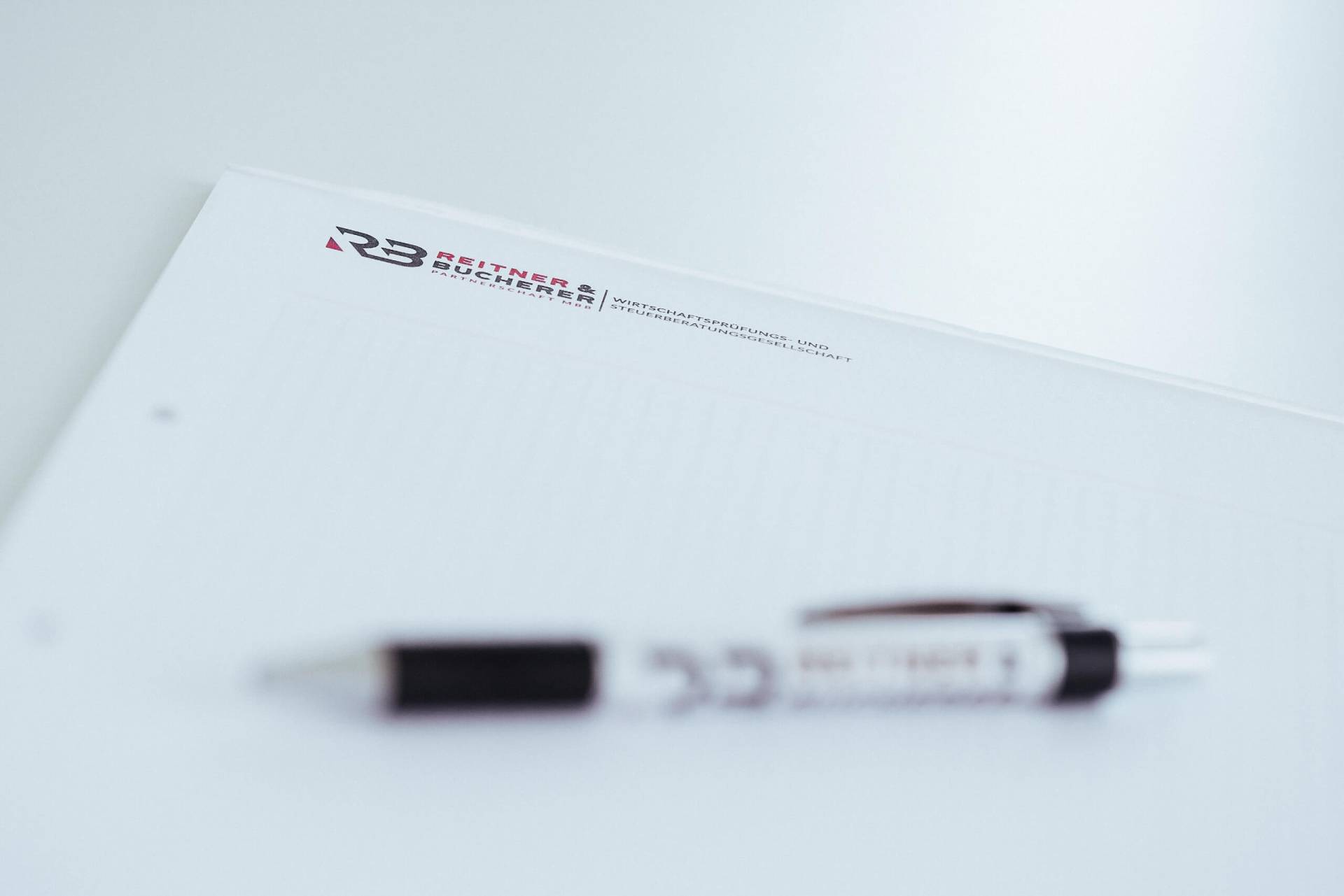 Foto: Schräg fotografierter Notizblock mit Briefpapier der Kanzlei Reitner & Bucherer (Logo oben) und einem leicht unscharfen Kugelschreiber im Vordergrund.